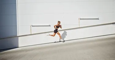Young sportswoman running outdoors against wall